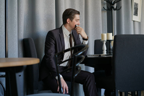 Trauriger Mann im Businessanzug, der mit einem Telefon in einem Café sitzt. er ist verärgert. - Foto, Bild