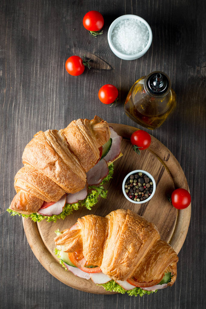 Croissant fresco ou sanduíche com salada, presunto, jamon, prosciutto, salame, queijo, frango, tomates em fundo de madeira. Conceito de pequeno-almoço. Alimentos saudáveis e rápidos
. - Foto, Imagem