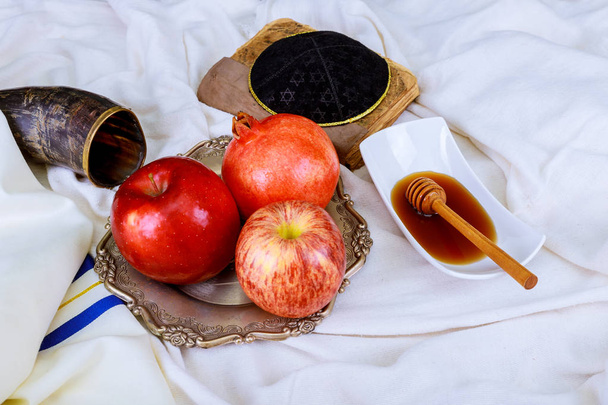 Ильхашана иудейская праздничная концепция - шофар, книга Торы, мед, яблоко и гранат поверх деревянного стола. традиционные праздничные символы. a kippah a yamolka
 - Фото, изображение