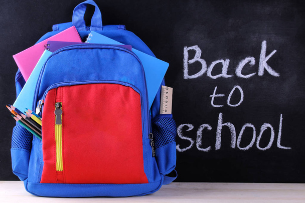 Schulrucksack mit verschiedenen Schulmaterialien auf dem Hintergrund einer Schultafel mit der Aufschrift zurück zur Schule - Foto, Bild