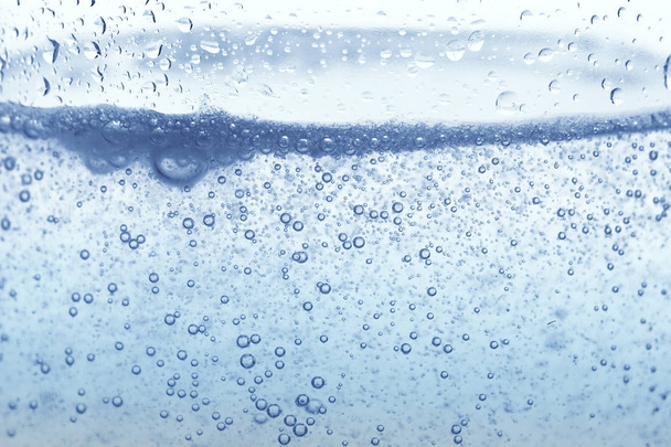 Φυσαλίδες οξυγόνου σε ποτήρι νερό σε μπλε φόντο. - Φωτογραφία, εικόνα