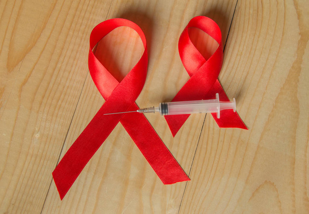 Κόκκινη κορδέλα ευαισθητοποίησης και συρίγγων σε ξύλινα φόντο: παγκόσμια ημέρα καταπολέμησης του Aids, προώθηση δημόσια υποστήριξη για την υγεία ανθρώπων που ζουν με Hiv τον Δεκέμβριο - Φωτογραφία, εικόνα