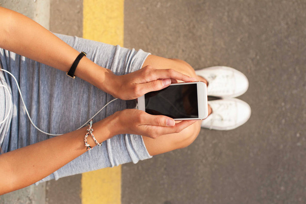 Girl in sneakers sitting on the floor with smart phone in her hands. - Foto, imagen