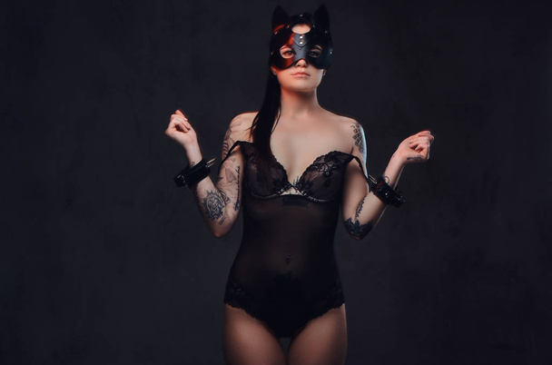 Seductora sensual amante chica con lencería negra en accesorios BDSM y máscara de cuero para gatos posando sobre un fondo oscuro. Aislado sobre un fondo oscuro
.    - Foto, imagen