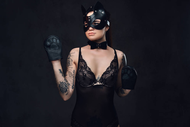 Kuuma brunette rakastajatar tyttö yllään musta alusvaatteet BDSM kissa nahka naamio ja tarvikkeet poseeraa tumma tausta
.  - Valokuva, kuva