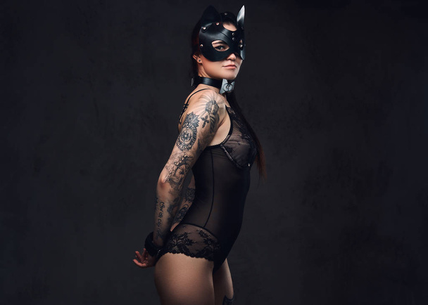 Chica amante morena caliente con lencería negra en BDSM gato máscara de cuero y accesorios posando sobre un fondo oscuro
.  - Foto, Imagen