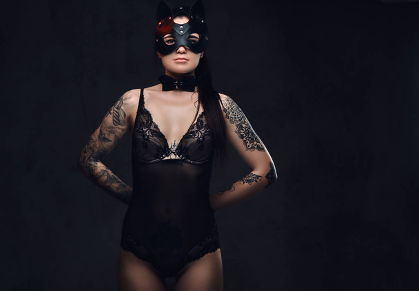 Seductive sensual mistress girl wearing black lingerie in BDSM accessories and cat leather mask posing on a dark background. Isolated on a dark background.    - Photo, Image
