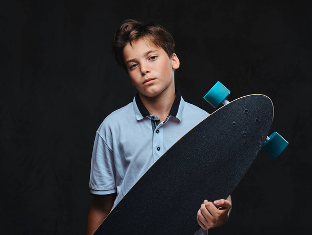 白い t シャツに身を包んだ若いスケーターの少年の肖像画は、ロングボードを保持しています。暗い背景に分離. - 写真・画像