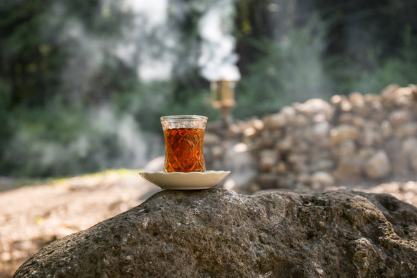Wschodniej czarnej herbaty w szkło na kamieniu w lesie. Herbaty wschodniej koncepcji. Armudu tradycyjnych Puchar. Tło zielony natura. Selektywny fokus - Zdjęcie, obraz