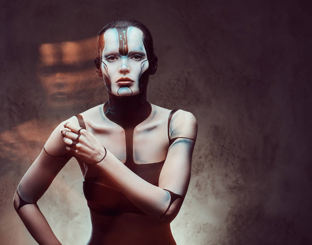 Retrato de cerca de una mujer cibernética con maquillaje creativo con efecto de luz posando sobre un fondo de textura oscura. Tecnología y concepto futuro
. - Foto, imagen