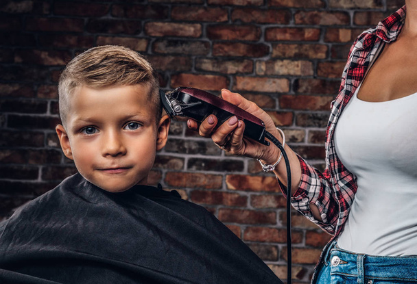 Retrato de cerca de un lindo niño en edad preescolar que se corta el pelo contra una pared de ladrillo
. - Foto, imagen