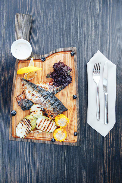 Жареная рыба на деревянной доске с овощами. деревянный фон. вид сверху
 - Фото, изображение
