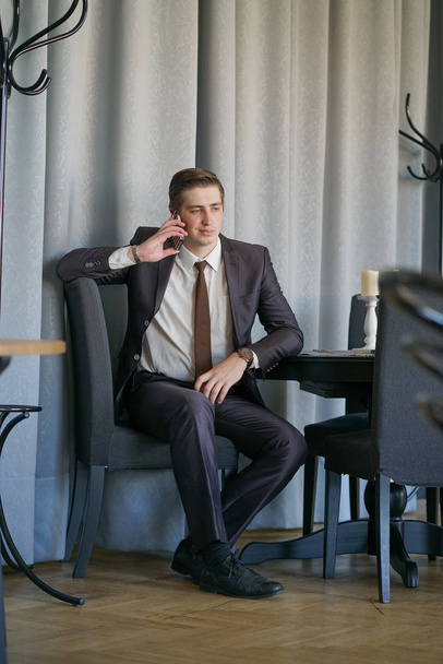 黒のビジネス スーツ、白いシャツとネクタイ冷静テーブルでカフェに座って携帯電話で話している若い男 - 写真・画像