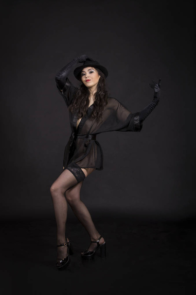 Beautiful young girl dancing in black tunic, black gloves and black hat.Posing in the Studio on a dark background, isolated images. - Fotó, kép