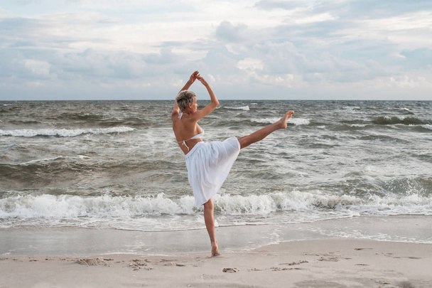 Young beautiful ballerina dancing and posing outside, sea background. - Фото, изображение