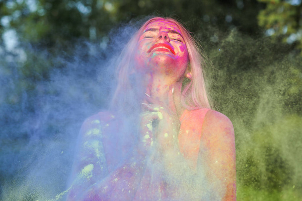 Γοητευτική ξανθιά γυναίκα με εκρηγνυόμενη πολύχρωμα χρώματα που γιορτάζουν το φεστιβάλ Holi - Φωτογραφία, εικόνα