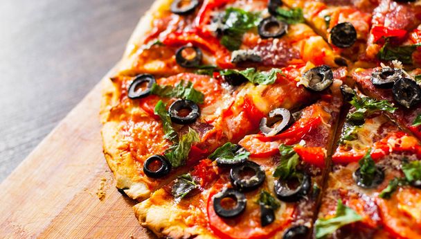 plasterki pizzy z ser Mozzarella, salami, papryka, pepperoni, pomidory, oliwki, przyprawy i świeżą bazylią. Włoskiej pizzy na podłoże drewniane - Zdjęcie, obraz