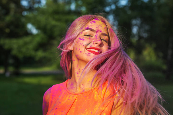 entzückende kaukasische Frau mit bewegtem Haar, die beim Holi-Festival mit farbenfroher trockener Farbe spielt  - Foto, Bild