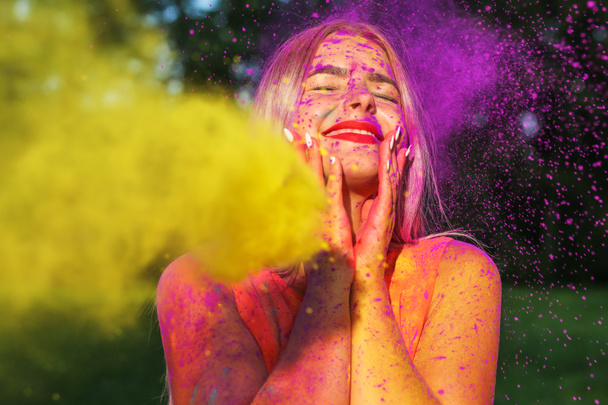 Vrolijke blonde meisje poseren met exploderende gele verf op Holi zomerfestival - Foto, afbeelding
