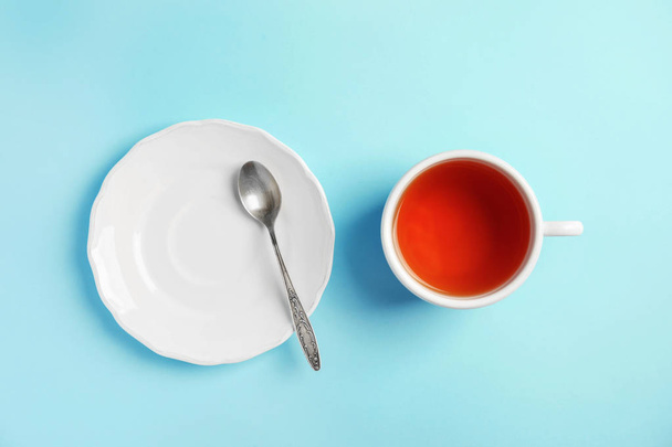 Cup of delicious tea with saucer and spoon on color background, top view - Foto, afbeelding