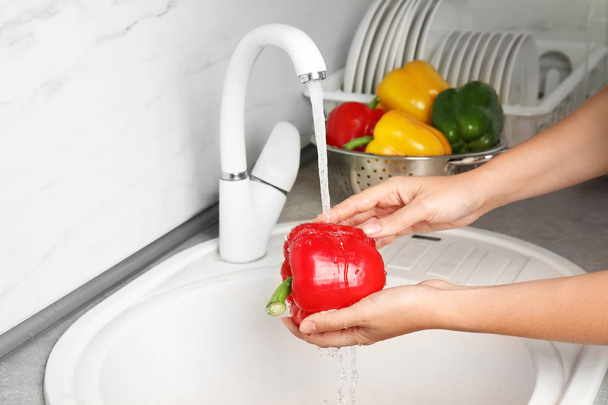 Woman washing paprika pepper in kitchen sink, closeup - Фото, зображення