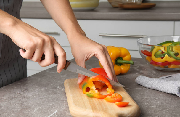 Woman cutting paprika pepper on wooden board at table, closeup - Photo, Image