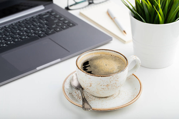 Bureau avec ordinateur portable, lunettes, bloc-notes, stylo et une tasse de café sur une table blanche. Fond clair
. - Photo, image