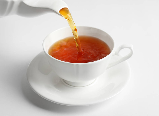 Pouring hot tea into porcelain cup on white background - Fotografie, Obrázek