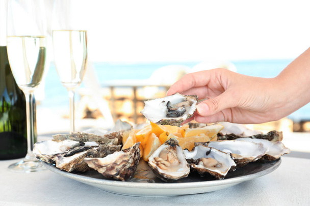 Woman holding fresh oyster over plate, focus on hand - Fotoğraf, Görsel