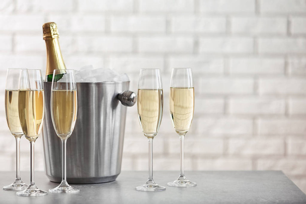 Glasses with champagne and bottle in bucket on table against brick wall - Foto, Imagen