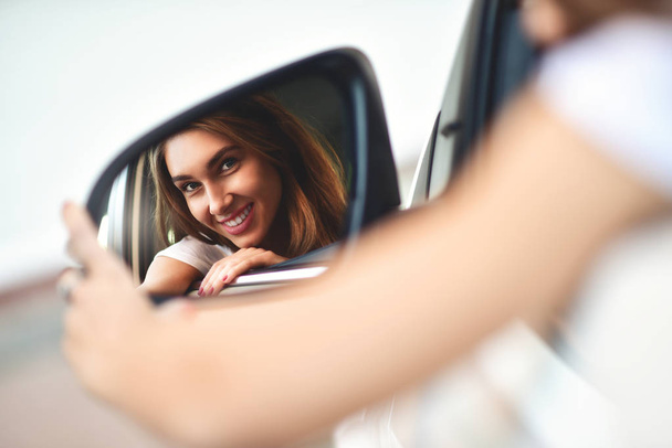 Retrato de linda chica sonriente sentarse en el .car y mirar el espejo del coche
 - Foto, Imagen