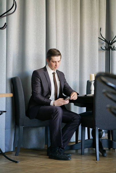młody człowiek w biznes czarny garnitur, biała koszula i krawat ogląda wiadomości w telefonie - Zdjęcie, obraz