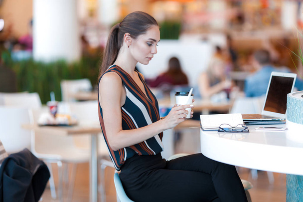 Mladá atraktivní dívka se sklenicí kávy v kavárně. Životní styl business portrét - Fotografie, Obrázek