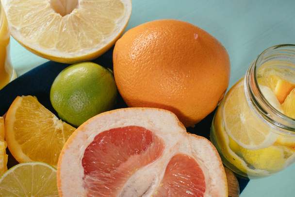 Zitrusfrüchte, Orangen, Zitronen, Limetten, Grapefruit, Pomelo auf Vintageplatte, Limonade und Saft im Glas vor türkisfarbenem Hintergrund - Foto, Bild
