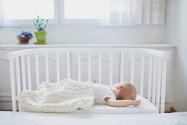 Adorable baby girl sleeping in co-sleeper crib attached to parents' bed. Little child having a day nap in cot. Infant kid in sunny nursery - Photo, Image