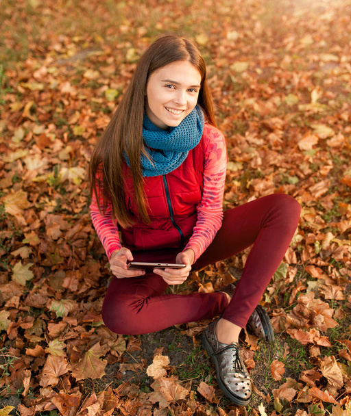 Bella ragazza che utilizza tablet all'aperto sdraiato sulle foglie e sorridente. Donna che utilizza tablet PC digitale nel parco autunnale. Studente che utilizza tablet dopo la scuola
. - Foto, immagini
