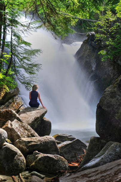 Mujer cerca de cascadas sentada sobre rocas. Vacaciones de primavera en Whistler. Rainbow Falls en Rainbow River. Parque Provincial de Garibaldi. Silbador. Columbia Británica. Canadá
. - Foto, Imagen