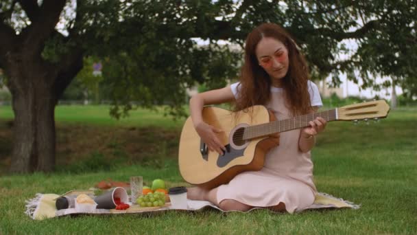 Krásná dívka hraje na akustickou kytaru v parku. - Záběry, video
