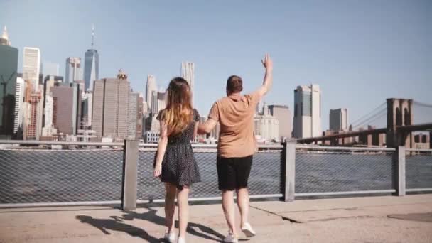 Happy European tourist couple run up holding hands arms raised to amazing Manhattan skyline, Brooklyn Bridge slow motion - Filmati, video