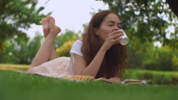 Mladá hezká žena pije kávu na trávě v letním parku. - Záběry, video