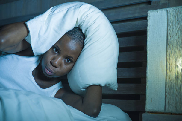 lifestyle night portrait of young desperate and stressed black afro American woman lying on bed upset trying to sleep suffering headache and hangover in insomnia and sleeping disorder problem - 写真・画像