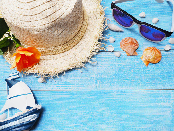 Holiday vacation background.Top view of straw hat, sunglasses, seashells and Chinese rose flower on blue wood with copy space.  - Photo, Image