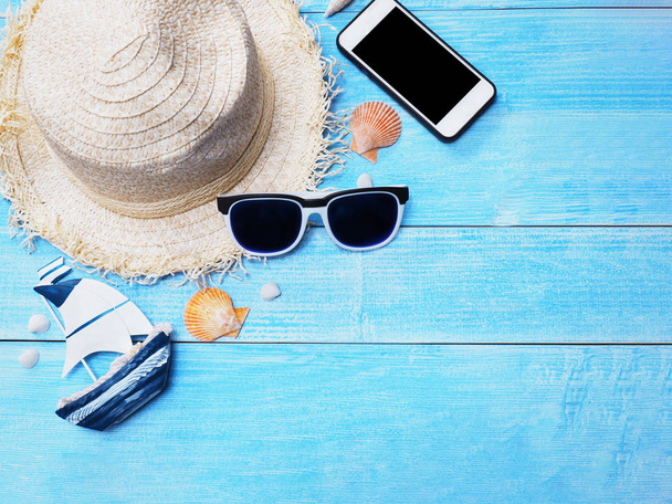 Holiday vacation background.Top view of straw hat, sunglasses, seashells and smartphone on blue wood with copy space.  - Фото, зображення