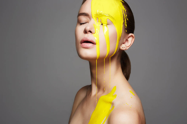 Νεαρή γυναίκα σε κίτρινο χρώμα. Υγρή μπογιά που ρέει πέρα από ένα όμορφο πρόσωπο και σώμα. Χρώμα Πορτραίτο κοριτσιού στη ζωγραφική - Φωτογραφία, εικόνα