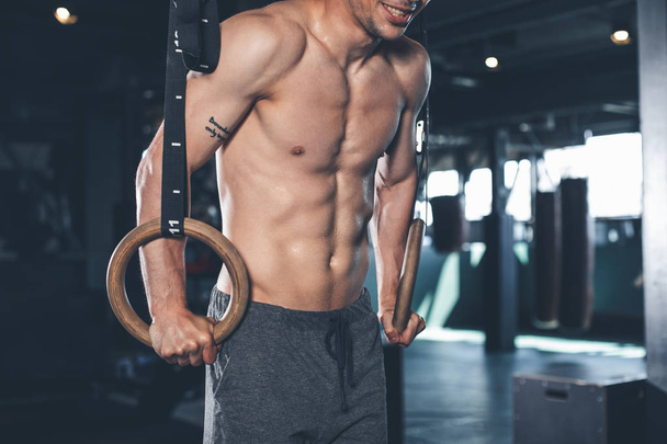 Smiling man is using gymnastic equipment for workout indoor - Foto, afbeelding