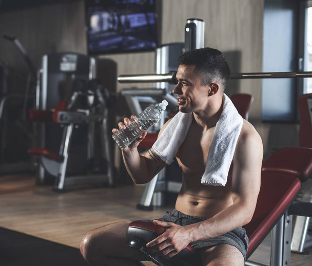 Positive bodybuilder is drinking water during interior workout - Fotoğraf, Görsel