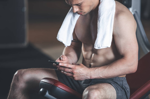 Calm sportsman is resting in gym with smartphone - Foto, Bild