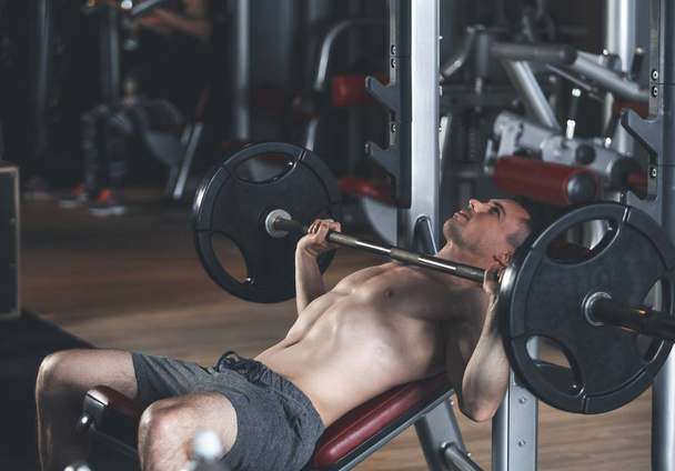 Concentrated man is lifting barbell in sport club - 写真・画像