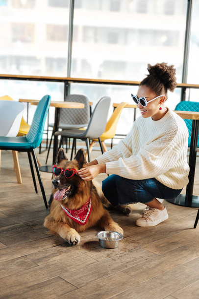 Funny curly woman putting bright sunglasses on her dog - Fotó, kép