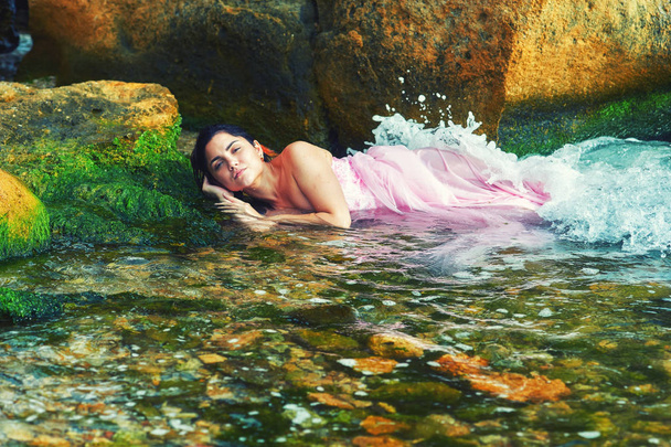Młoda dziewczyna leżąc w wodzie w różowej sukience . - Zdjęcie, obraz